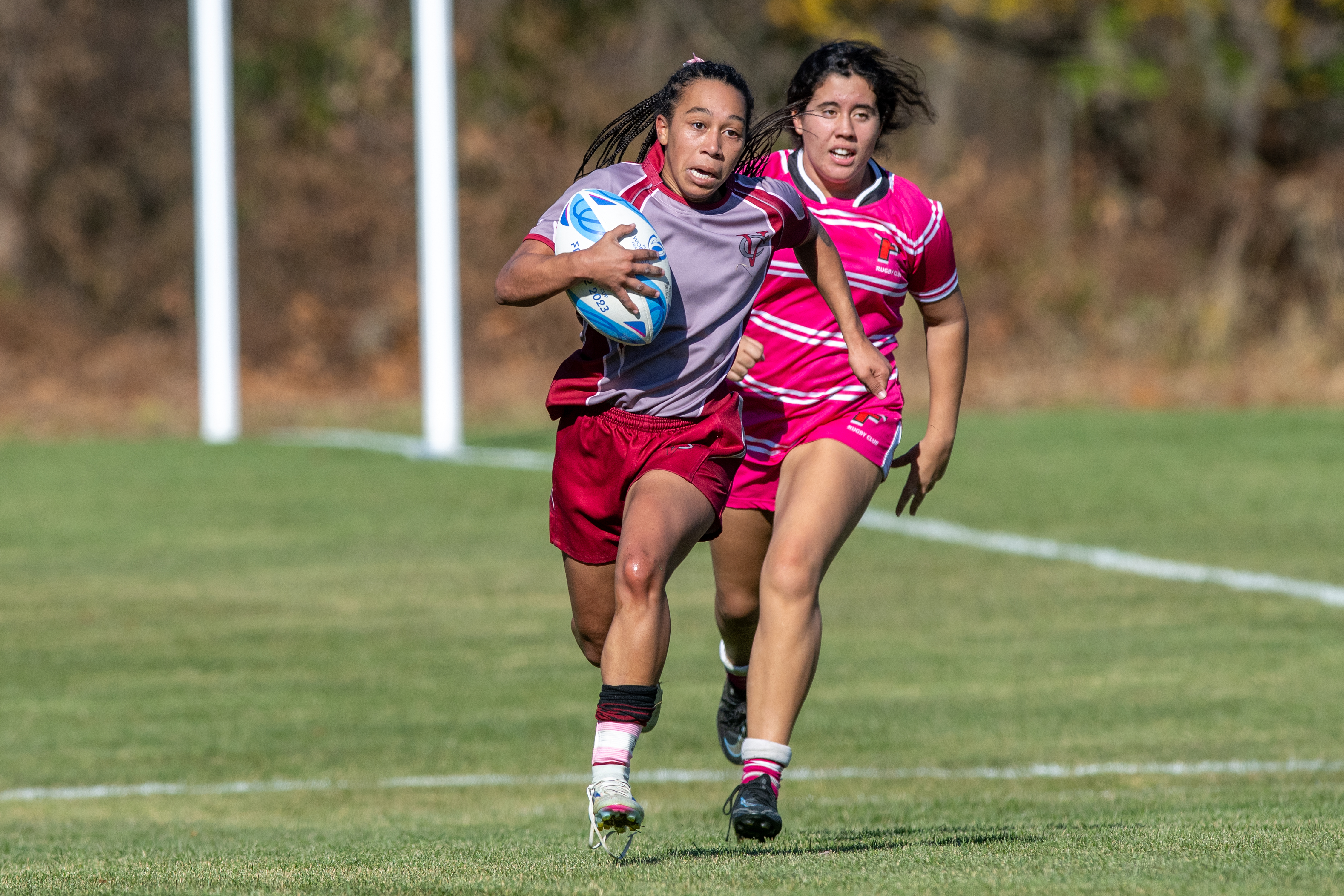 A rugby player runs with the ball, closely pursued by an opposing player.