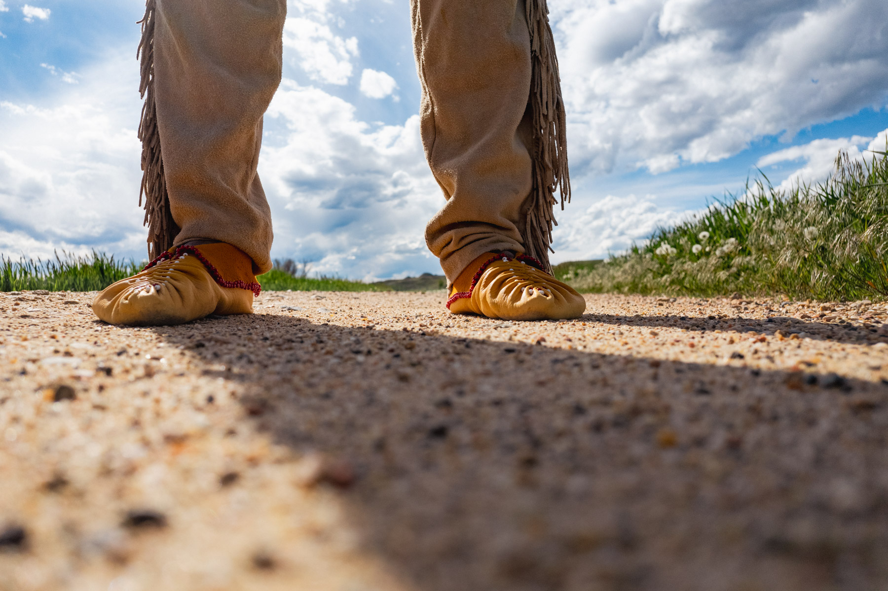 Close up of two feet wearing traditional moccasins standing on pavement 