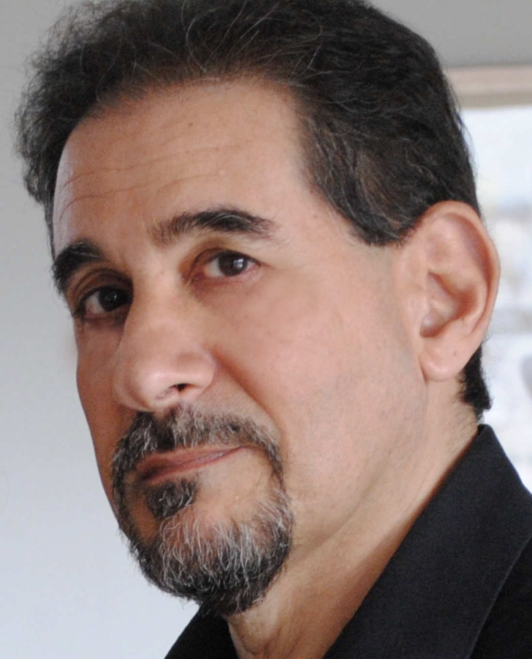 A photo of John Masto, a person with dark hair, dark facial hair, and a black shirt.