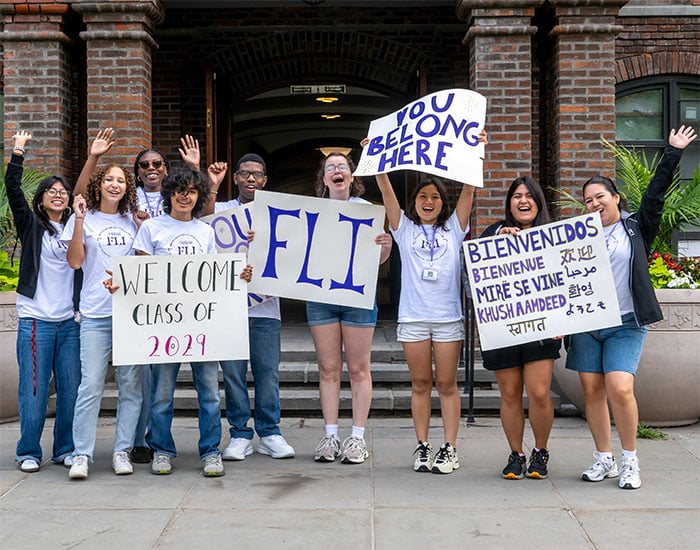Group of students holding welcome signs, incluFLI” and “You Belong Here,” outside a campus building.