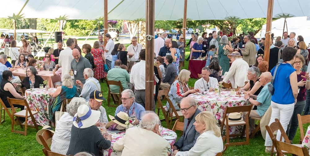 A large group of people sit at tables under a tent.