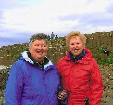 Two people wearing blue and red waterproof jackets pose in front of a rock wall.