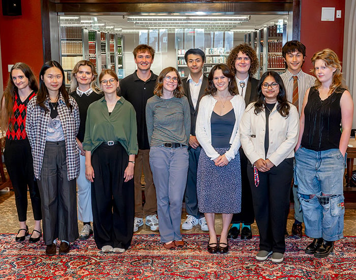 A small group of Vassar students standing together indoors in front of bookshelves, smiling at the camera.