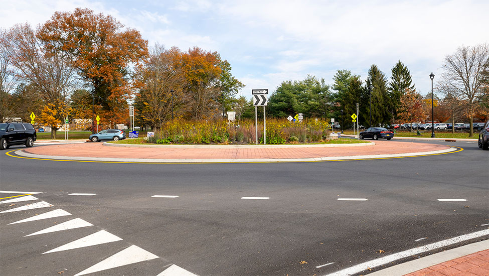 A newly constructed roadway with a large roundabout and autumn trees in the background