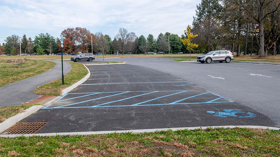 A newly constructed parking lot with two silver cars parked in it and autumn trees in the background.