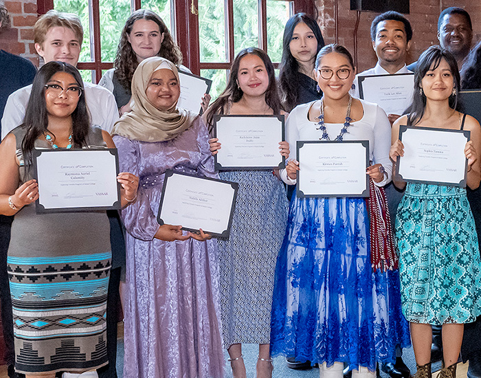 A group of people standing indoors, holding certificates and smiling at the camera.