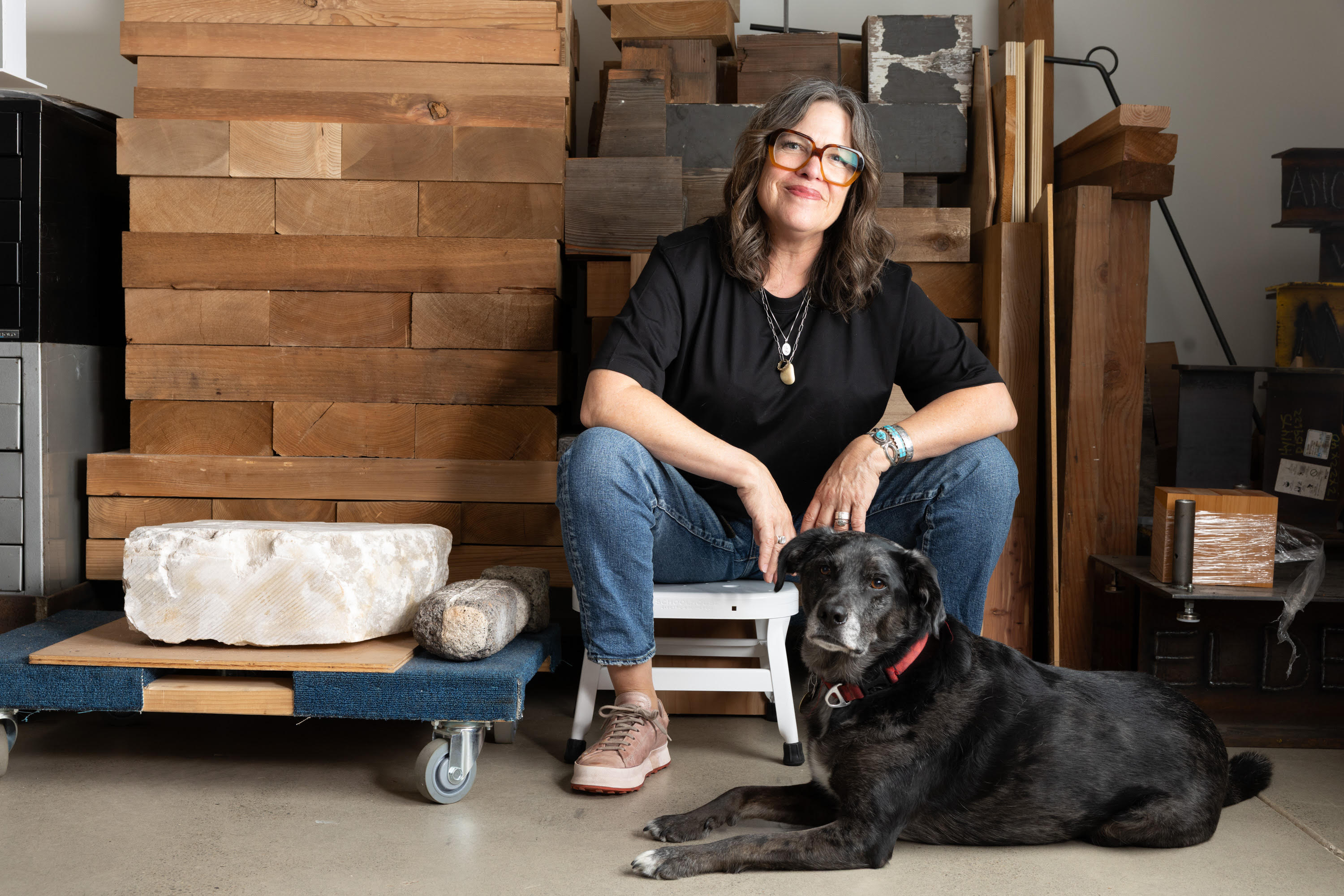 Artist Marie Watt seated in her studio with a dog resting at her feet