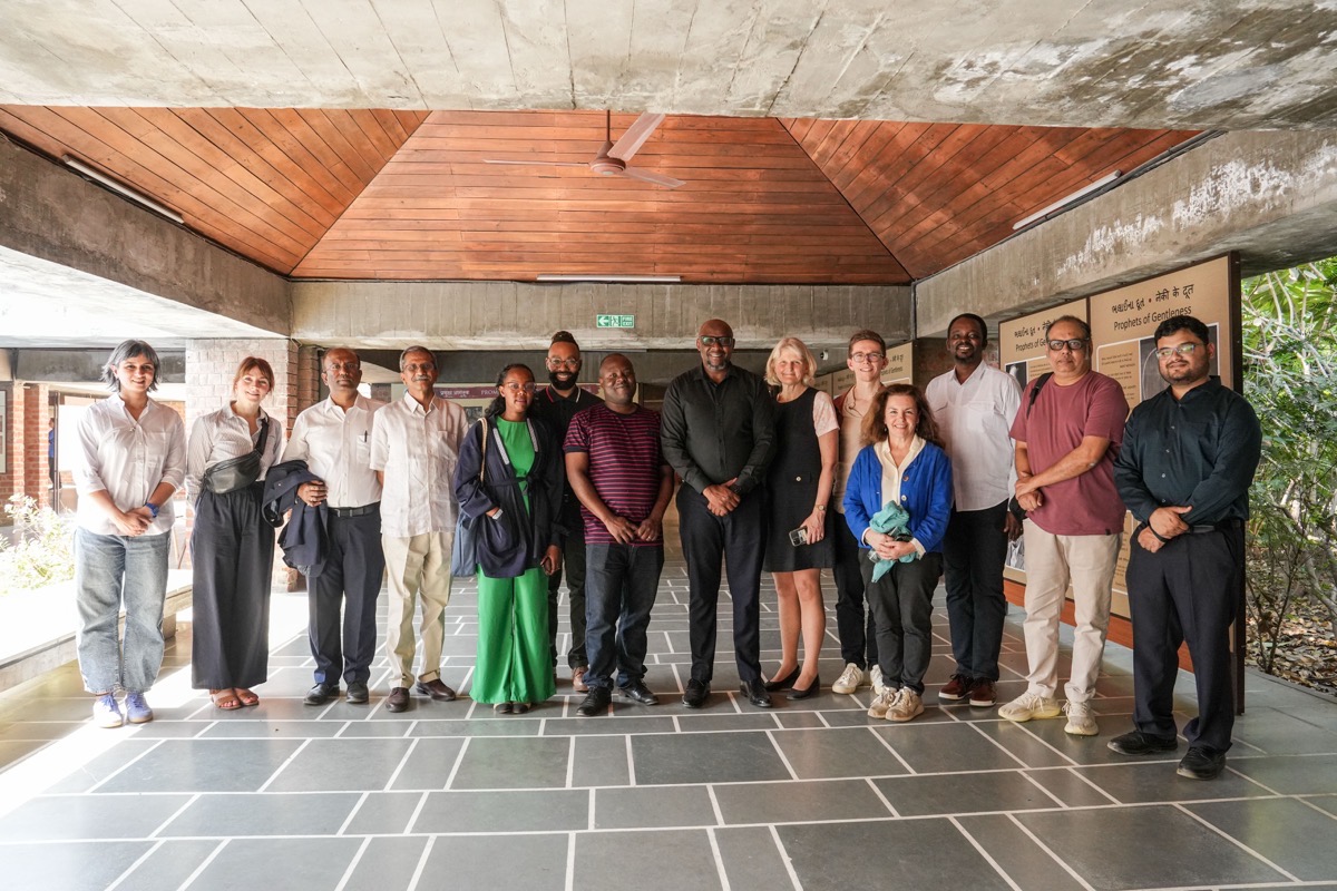 A group of people stand in a space with a roof but open on the sides.