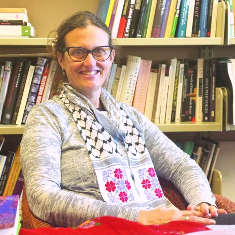 Portrait of subject casually sitting in an academic office with shelves of books in the background.