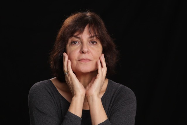 Portrait of subject with hands on the sides of their face with a dramatic dark background.