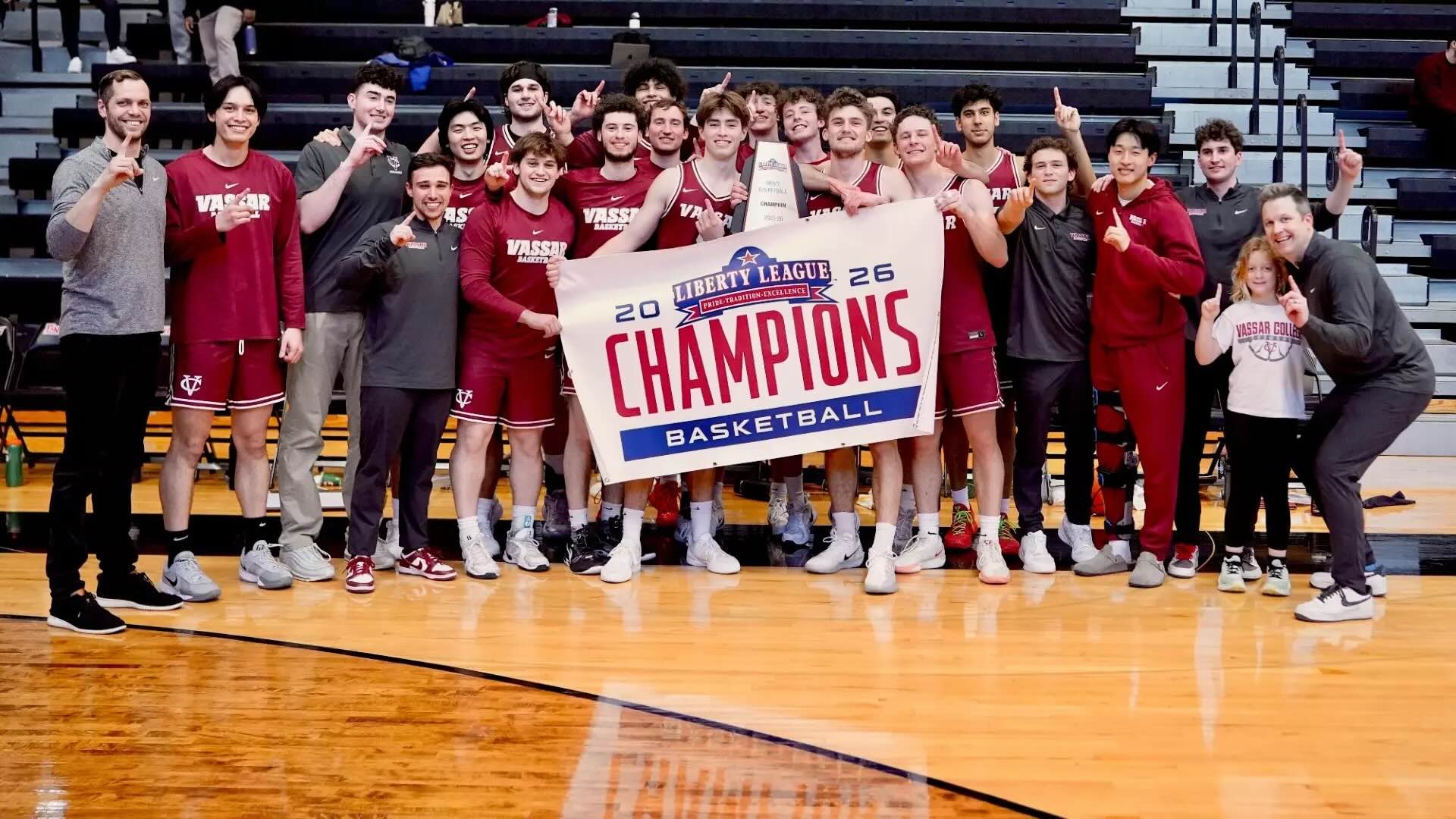 Basketball team on the court, holding a championship banner and posing for a photo.