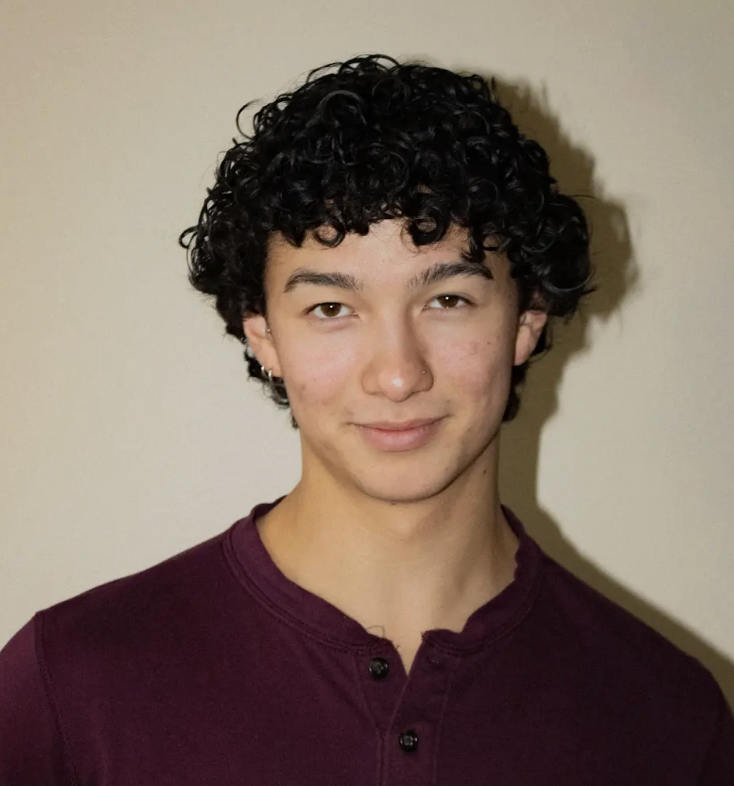 A portrait of Nikko Ramos, a person with a maroon shirt and short curly black hair.