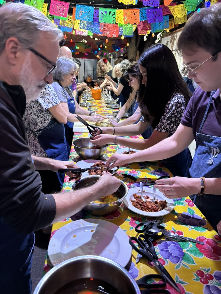 People line up on either side of a long table, preparing food in an assembly-line.