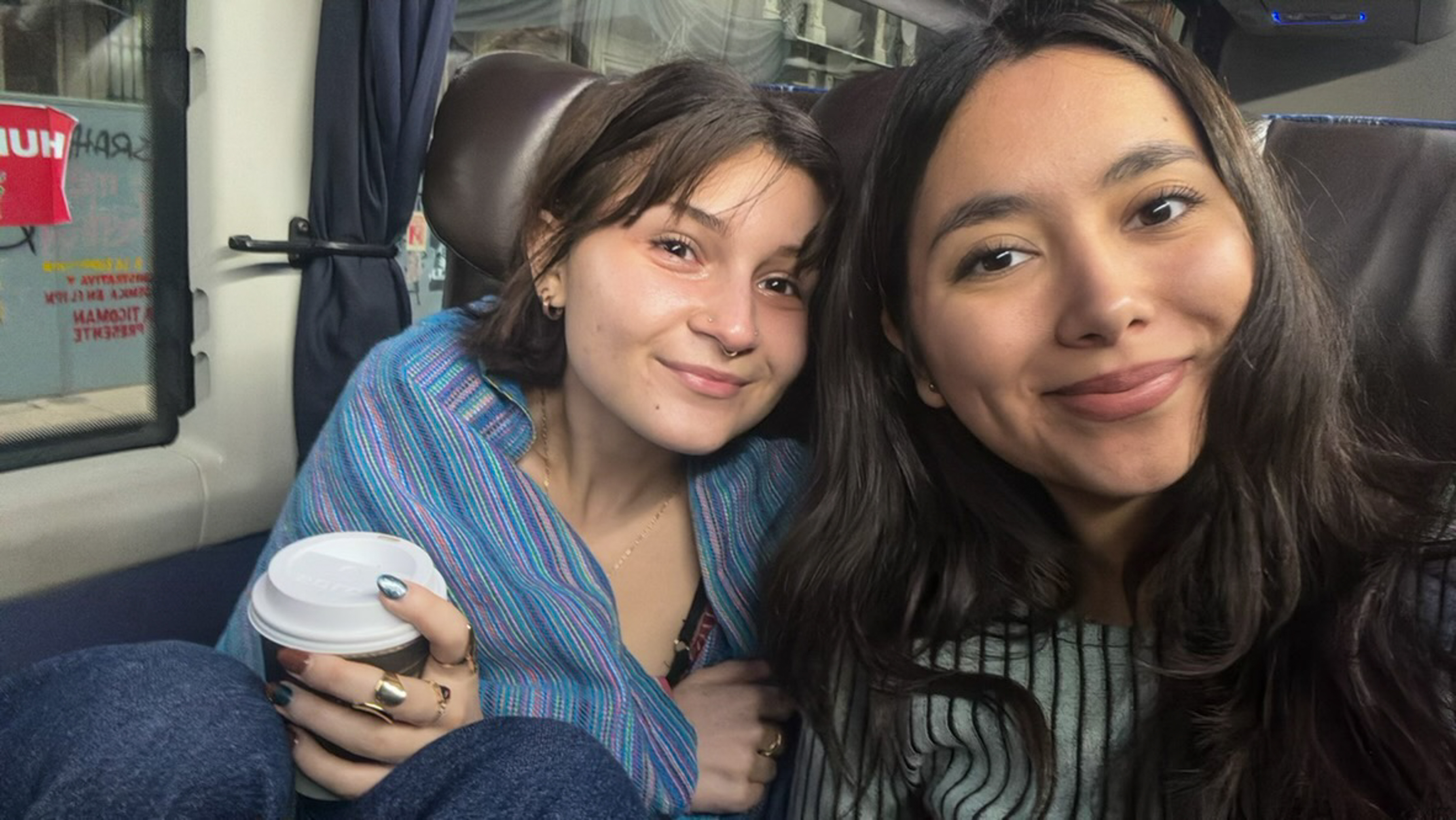 Two woman drink coffee while traveling on a train.