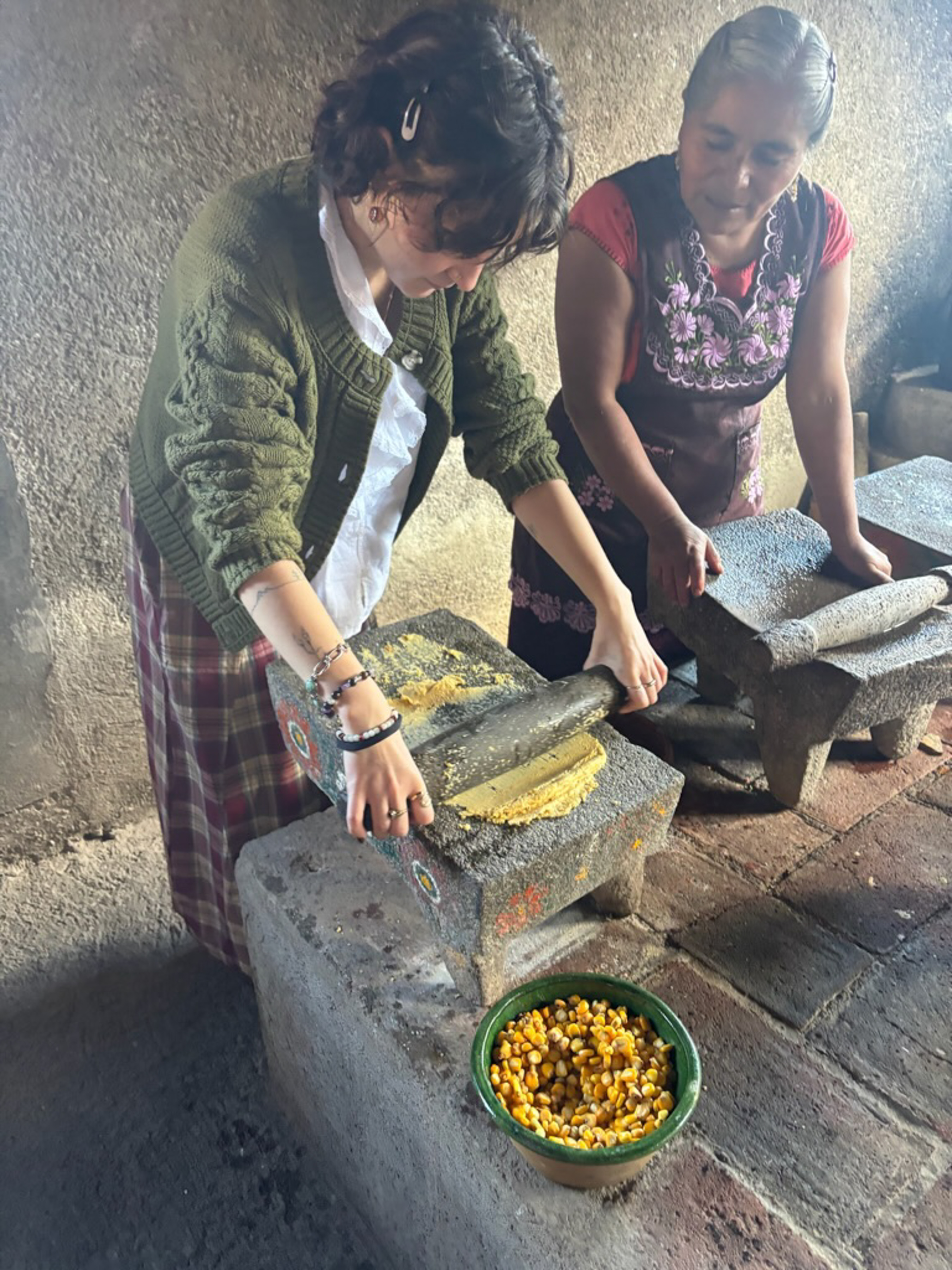 A younger woman is shown how to make tortillas by an older woman.