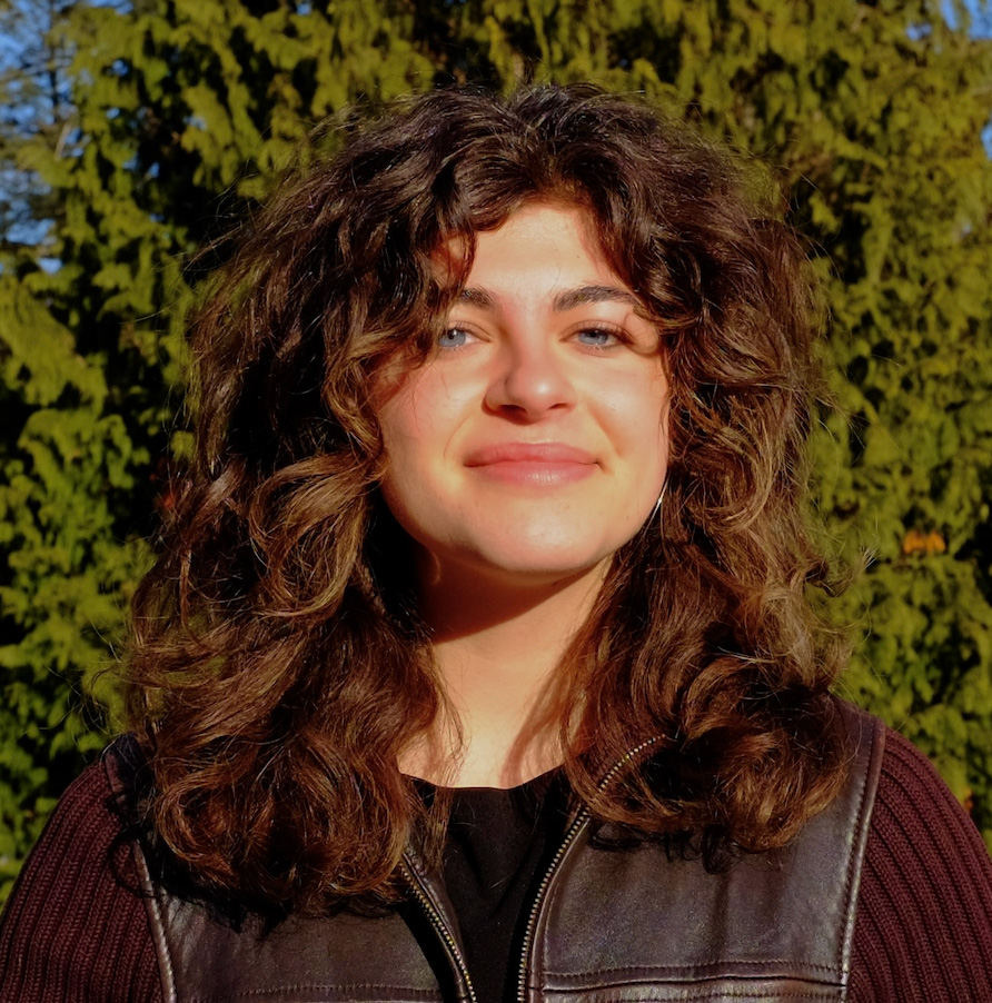 Avery Epstein smiles warmly in an outdoor portrait, with trees in the background.