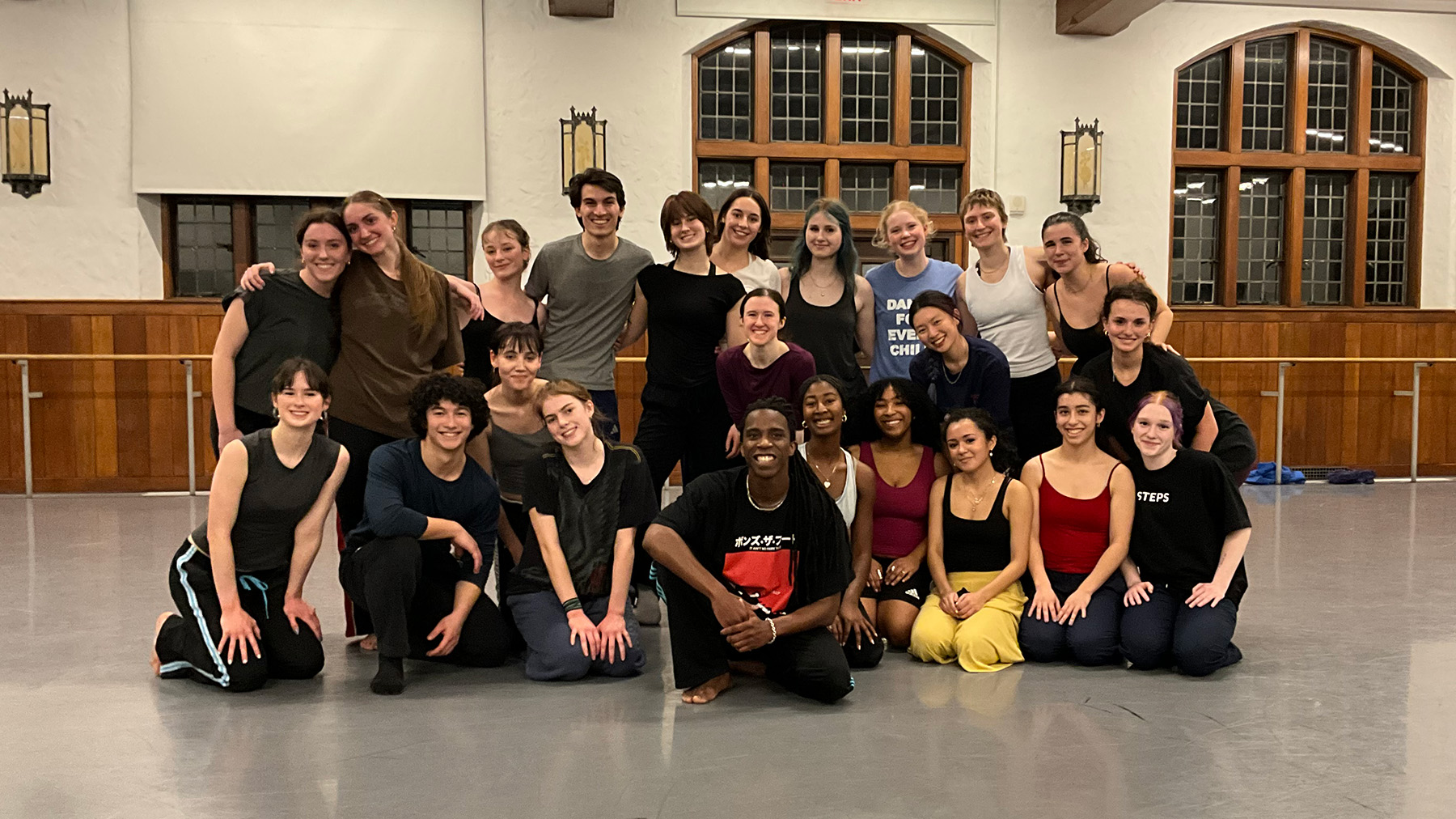 A group of dancers posing together in a studio, smiling and gathered in rows after a rehearsal.