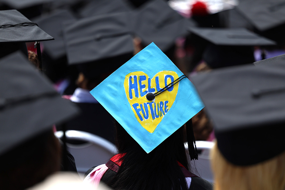 A close up view of the black caps of a group of graduates, with one cap in the center painted light blue with a yellow heart that says "HELLO FUTURE."