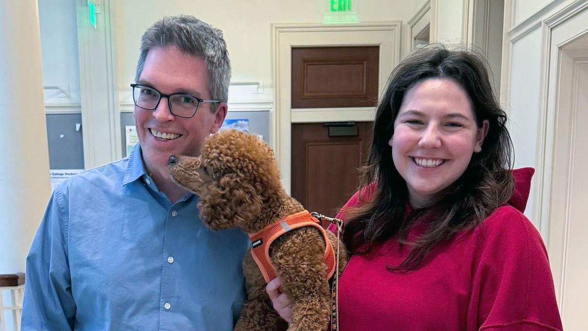 Two smiling people holding a dog.