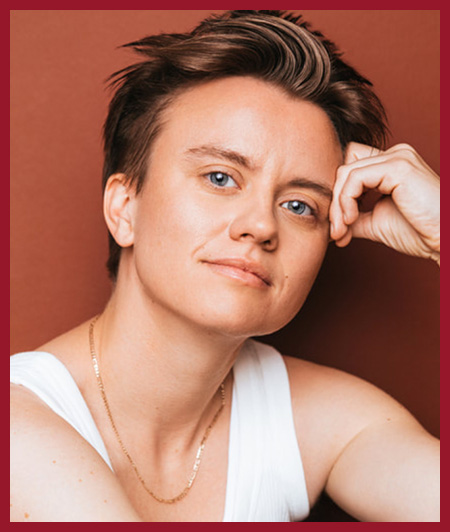 Portrait of a person resting their head against one hand, wearing a light-colored sleeveless top, posed against a warm-toned background.