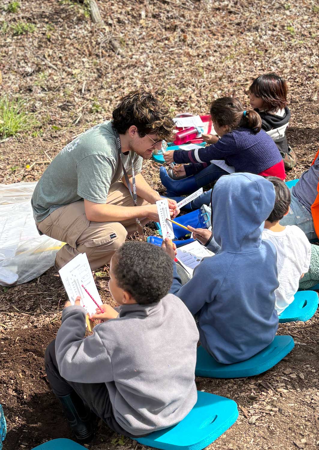 School age children with teacher in the field looking at thermometers.