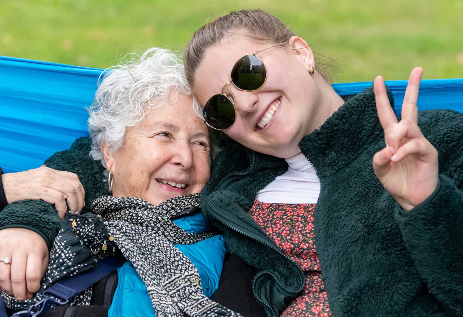 Two smiling seated people arm in arm; one person is making a peace sign.
