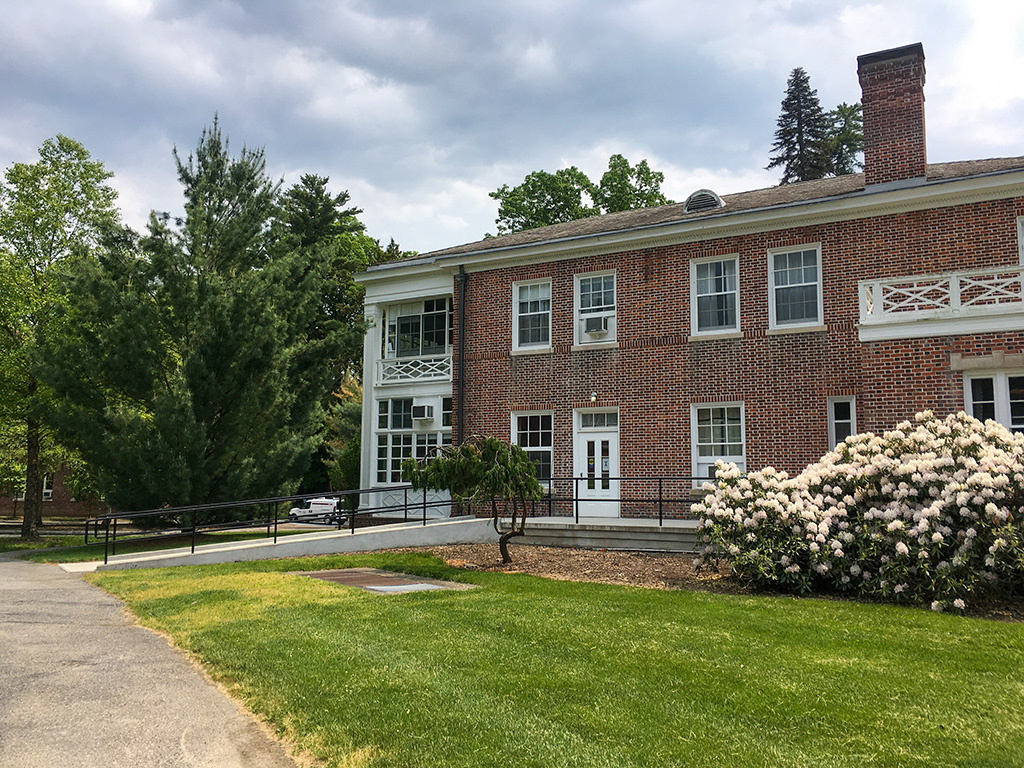 The side of a red brick building with a large chimney, a white porch, and a wheelchair ramp.