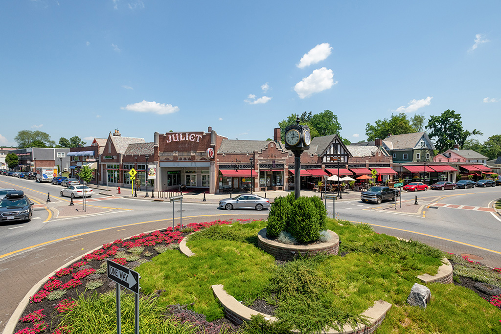 A clock on a pole in front of a street. In the center of the background is a building with a large sign, "Juliet".