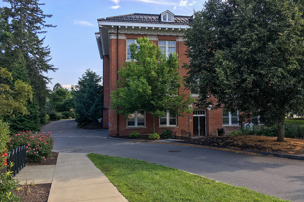 A brick building with trees and a sidewalk.