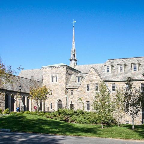 Skinner Hall of Music, a stone building with a tall central spire, viewed across a landscaped lawn under a clear blue sky.