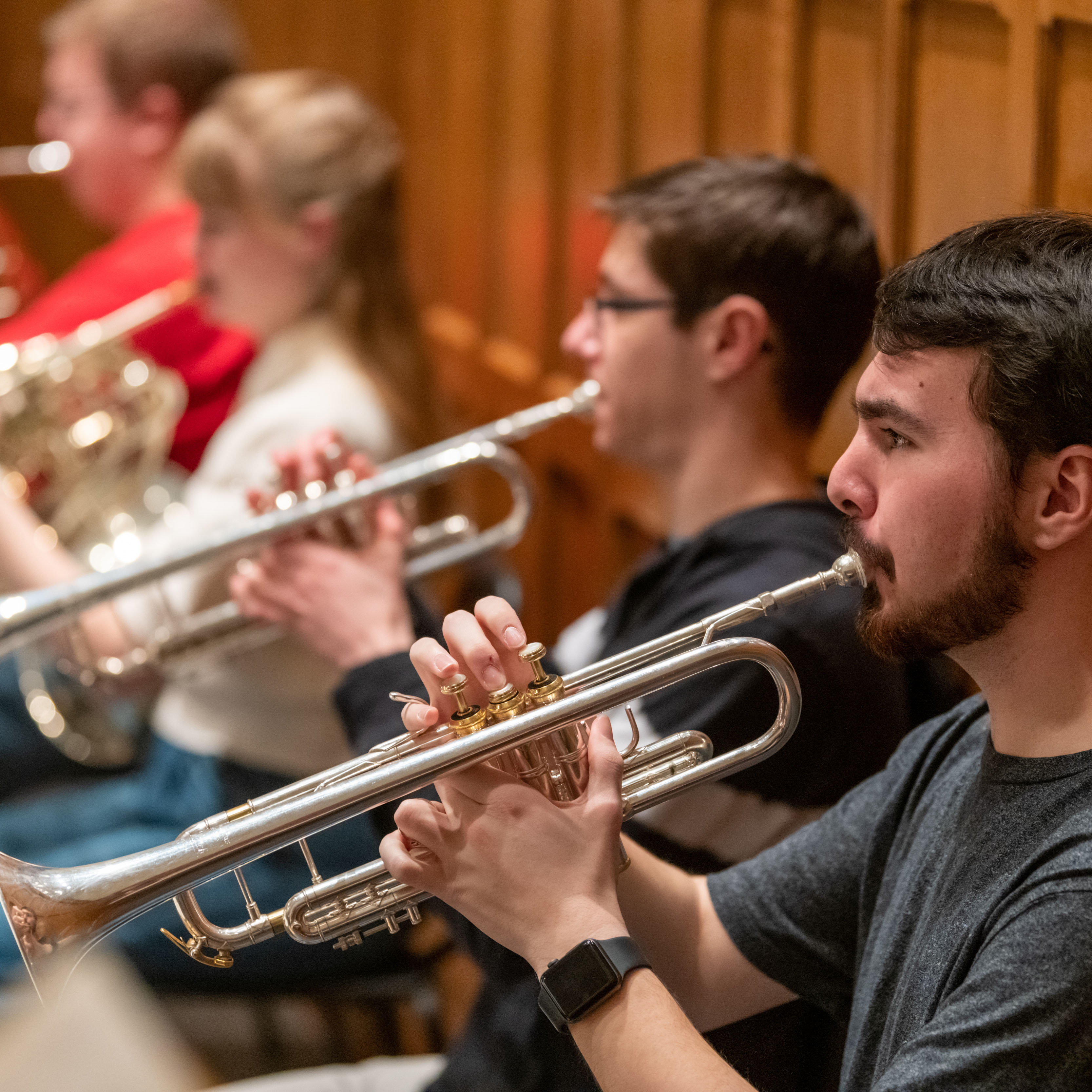 Student musicians play trumpet and other brass instruments during an orchestra performance.