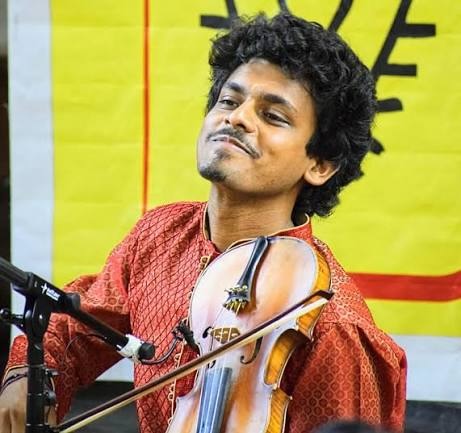 Sumanth Manjunath performs on violin while wearing a red patterned kurta.