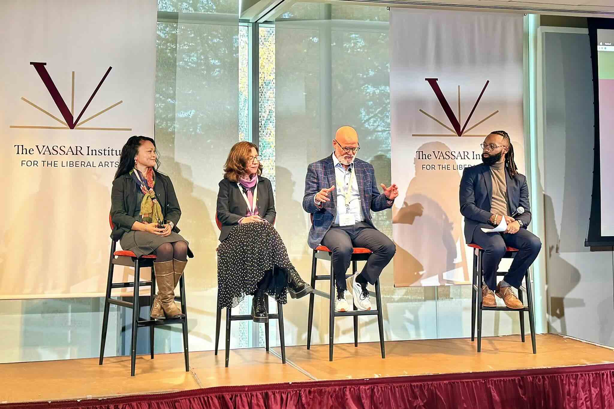 A group of people sit on chairs on a stage during an event.