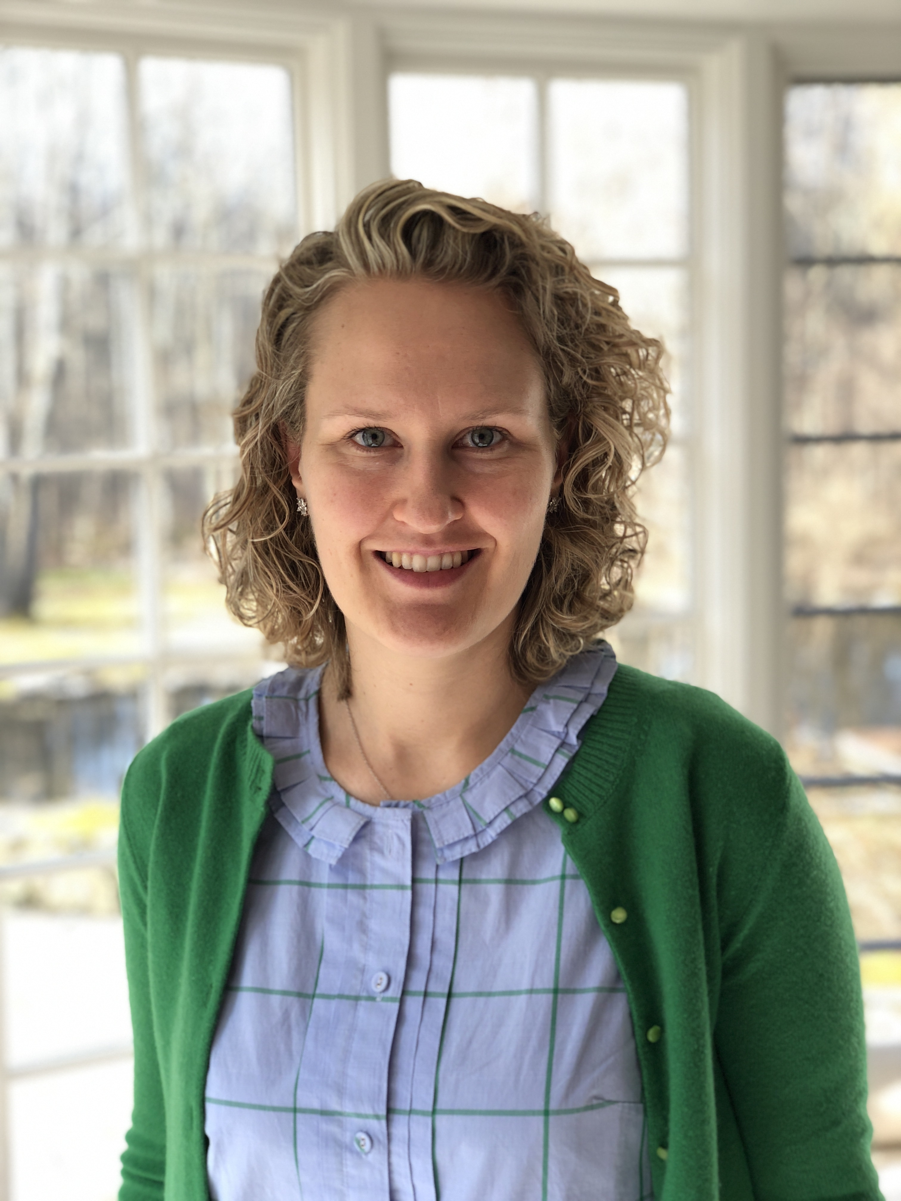 A photo of scholar Christina Weyl smiling and standing in front of a window.