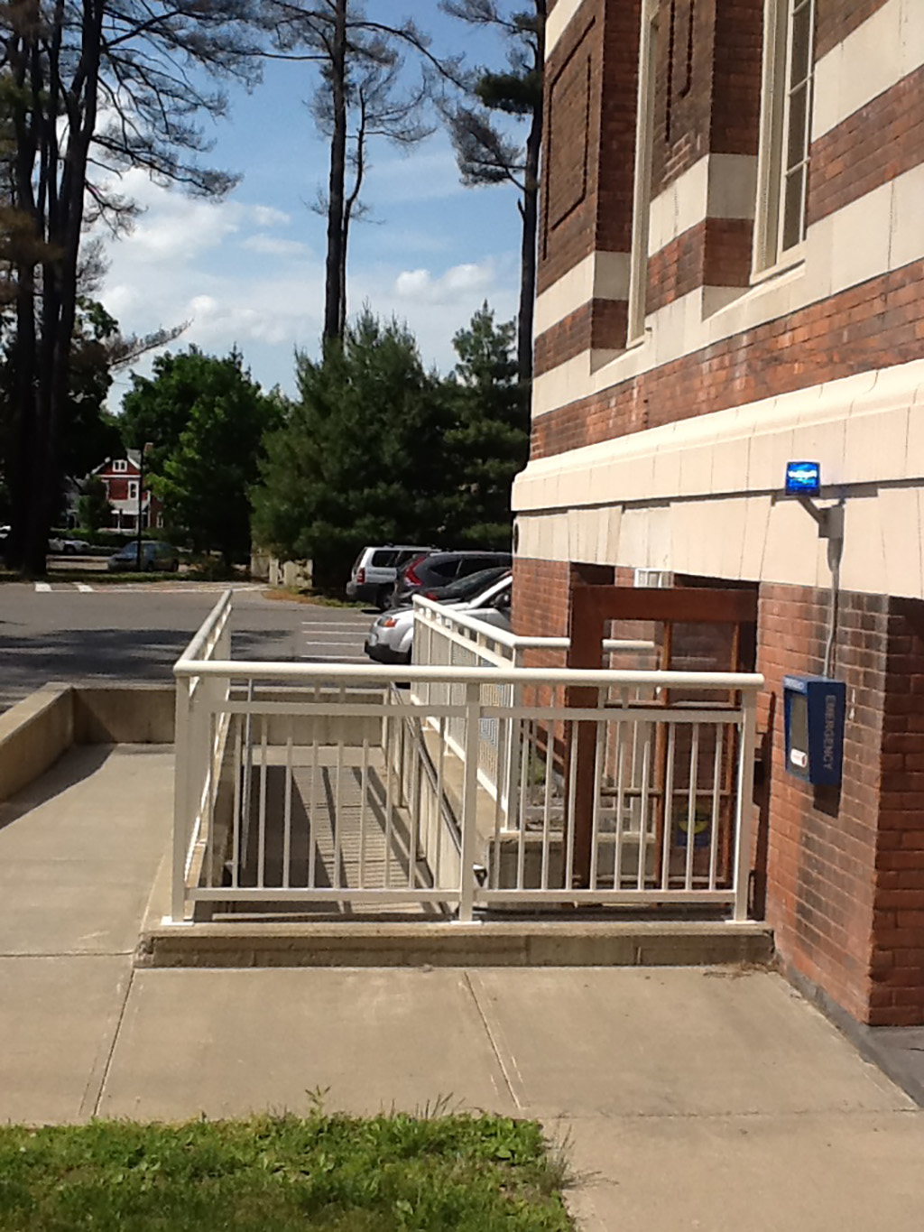 A ramp with a white railing on a brick building near a parking lot.