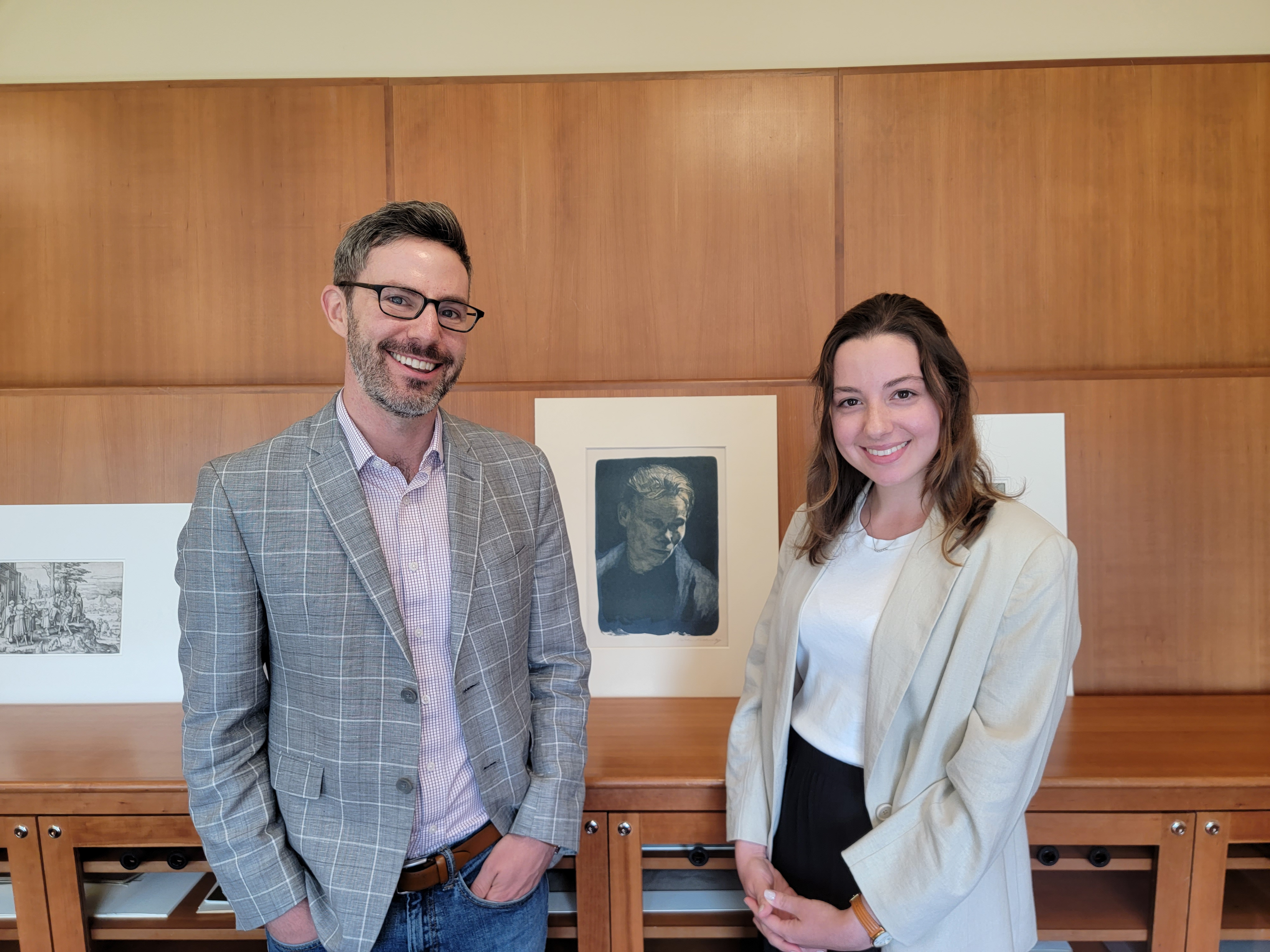 John Murphy and Ruby Funfrock stand in the Loeb's Print study room, with prints on the shelf behind them.