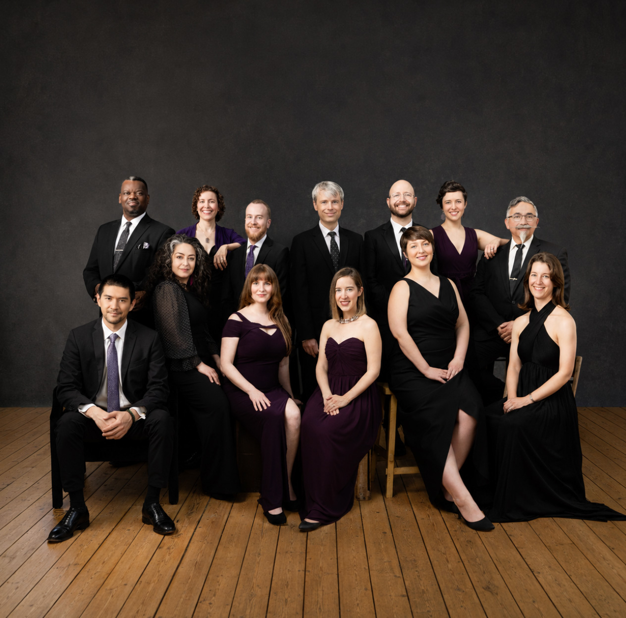 Members of the Skylark vocal ensemble pose together in formal attire against a dark studio backdrop.