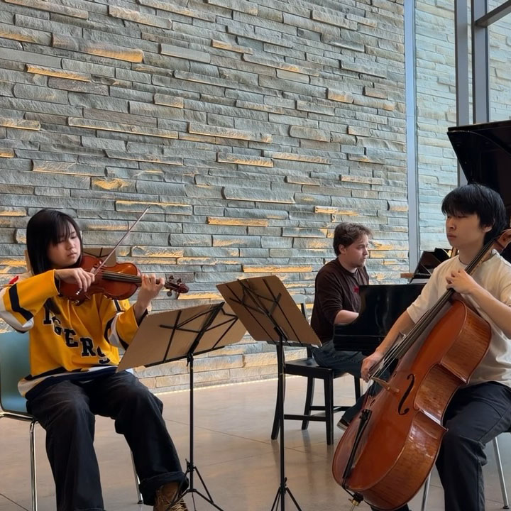 Three student musicians perform on violin, cello, and piano in the Bridge for Laboratory Sciences.