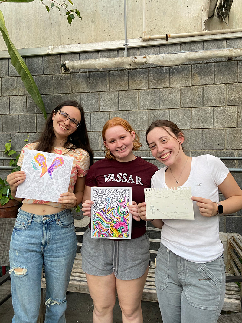 Three people standing in a greenhouse and displaying their completed artwork.