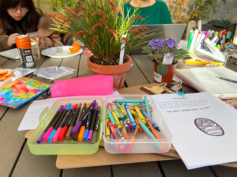 Art supplies, coloring pages, and potted plants arranged on a table during a greenhouse activity.