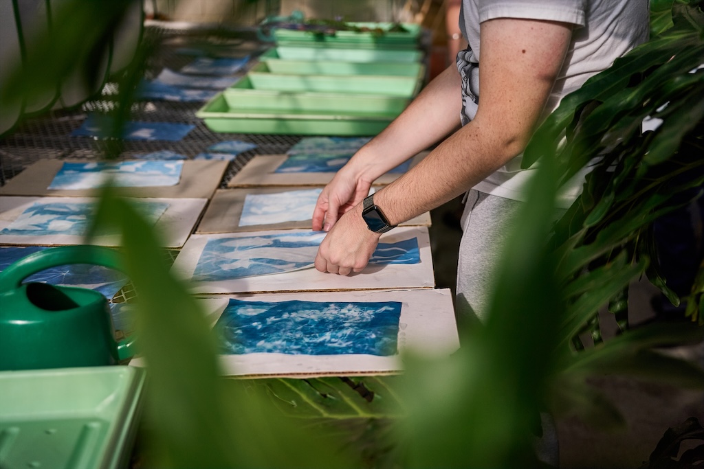 Detail of a table with pages of blue images with someone in the center placing one down on the table.