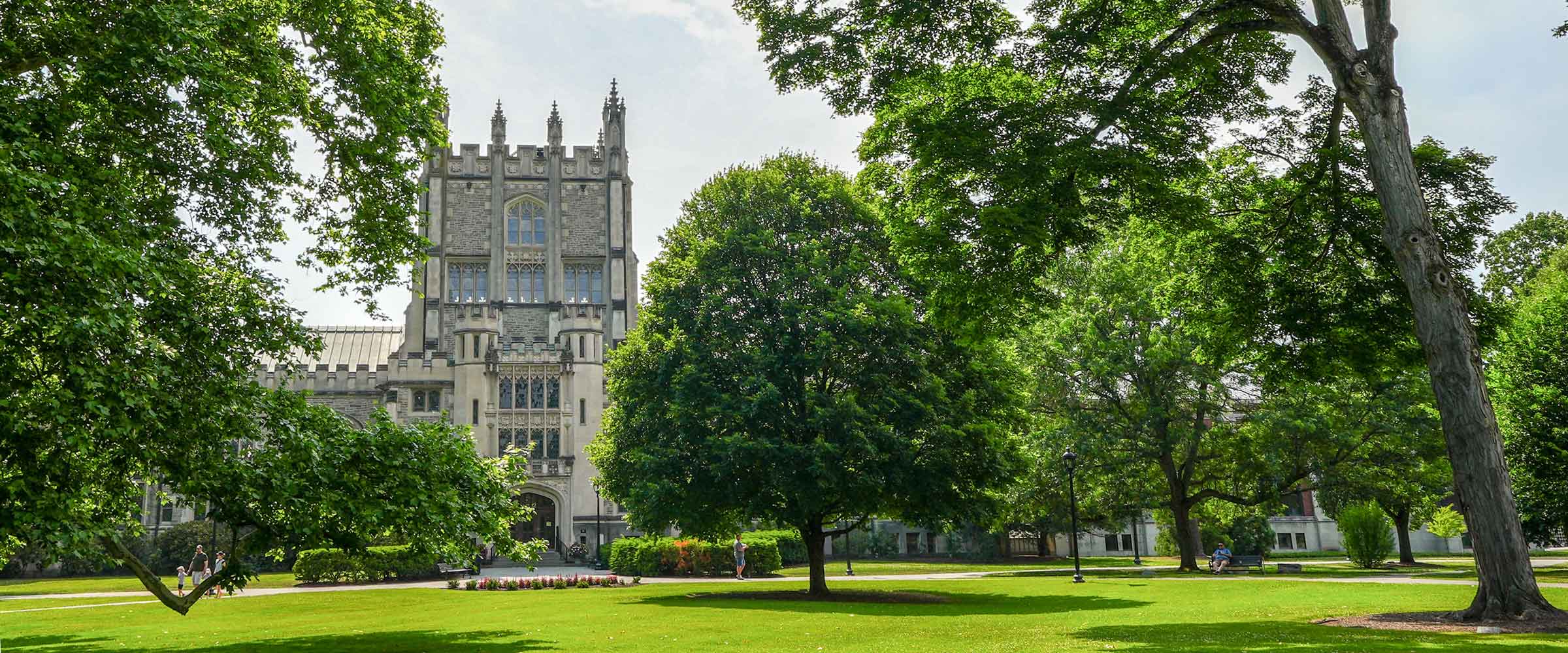 Building nestled among trees behind a large green lawn on a sunny day.