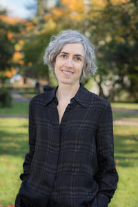 Smiling person with short gray hair, photographed outdoors.