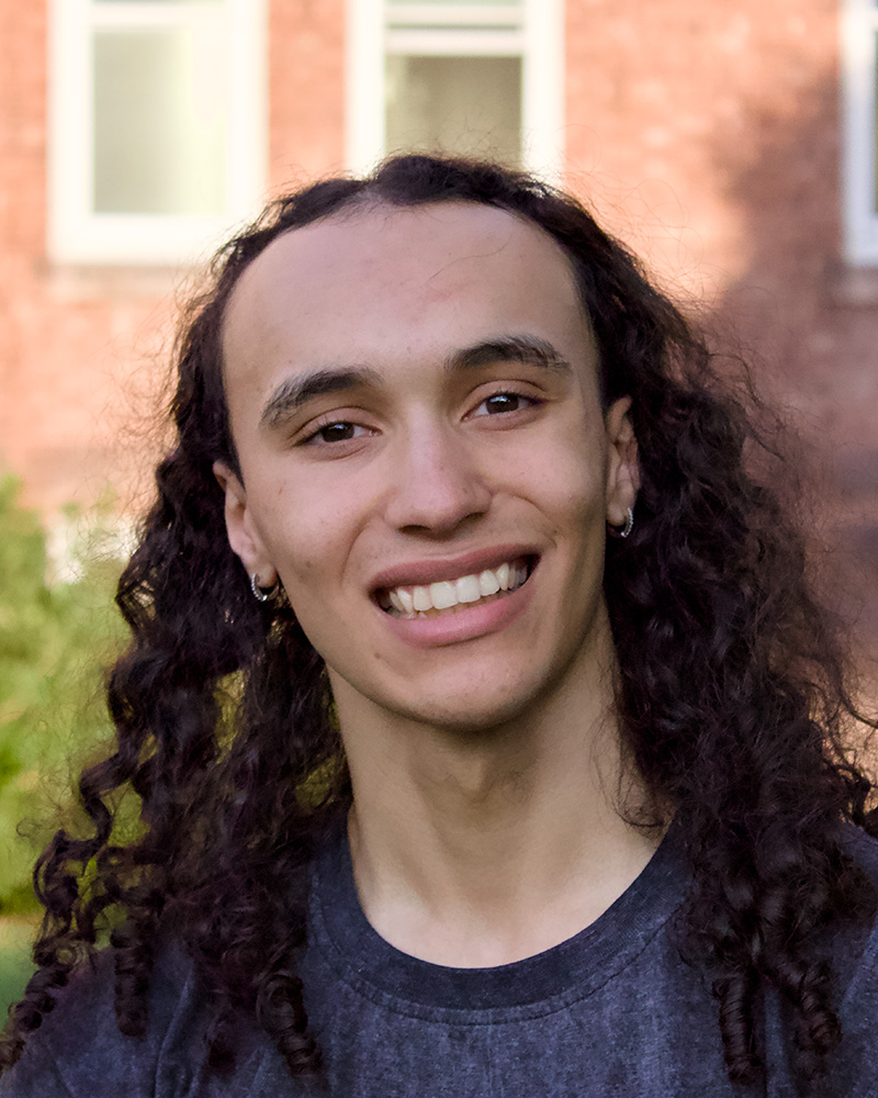 Smiling portrait of a student outdoors with a brick building in the background.