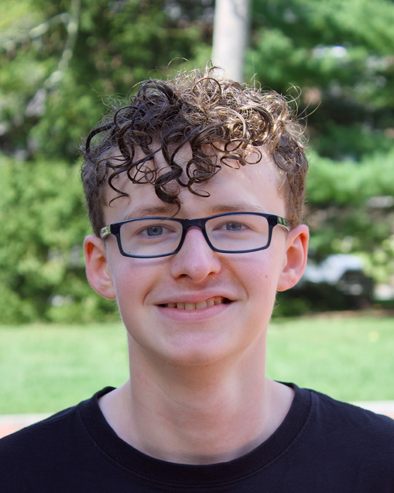 Smiling portrait of a student outdoors with trees in the background.
