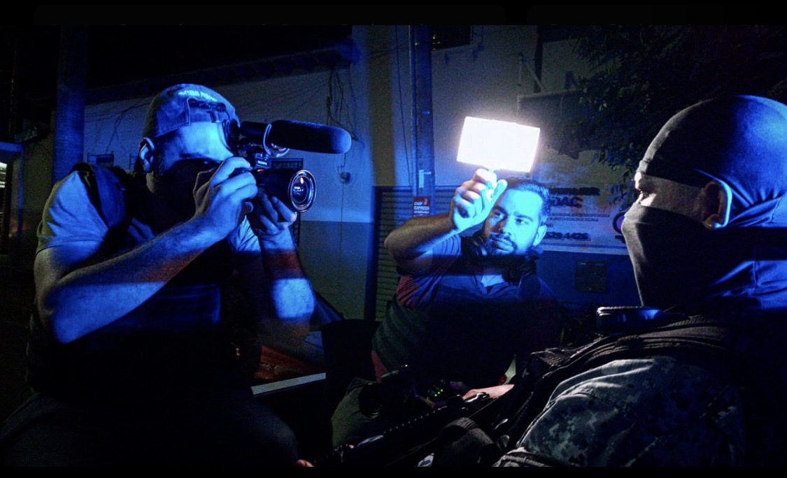 Camera crew films a masked person at night under blue lighting.