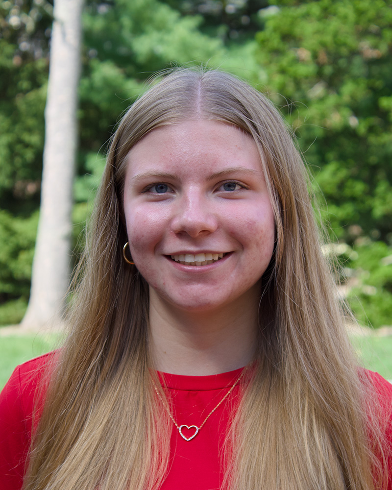 Smiling portrait of a student outdoors with trees in the background.