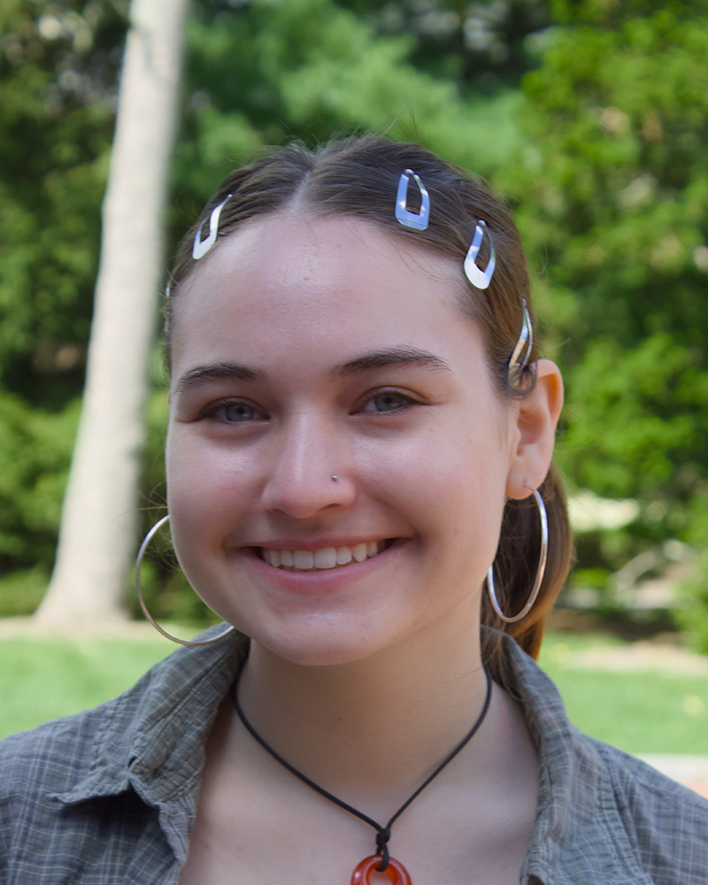 Smiling portrait of a student outdoors with trees in the background.