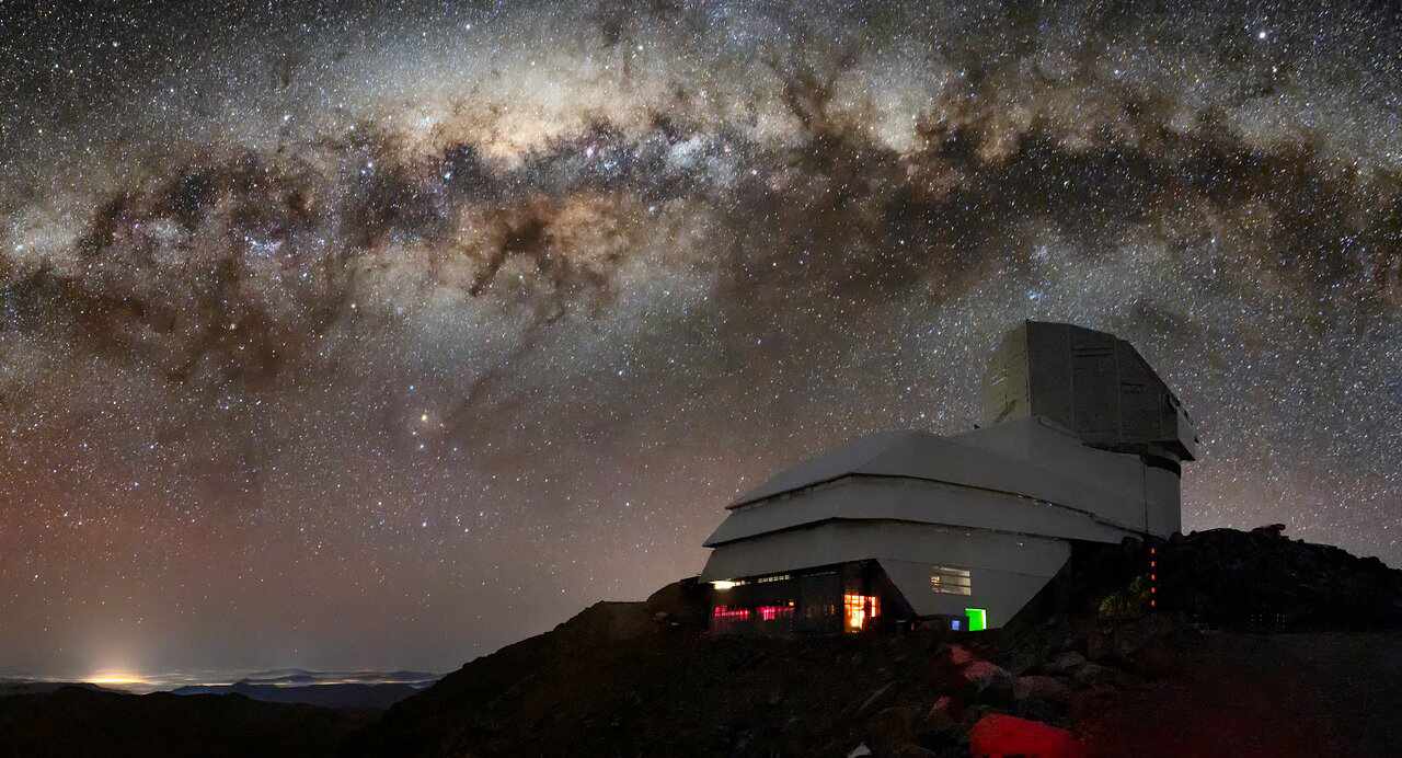 An observatory sits against a starry night sky, a galaxy visible in the background.