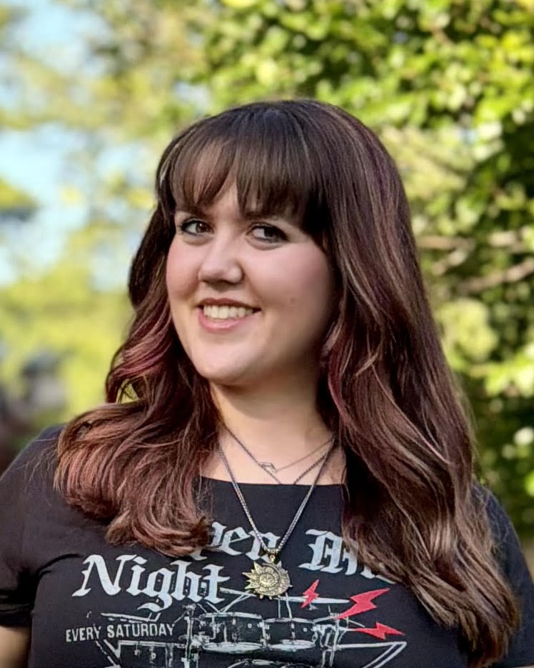 Smiling portrait of a student outdoors with trees in the background.